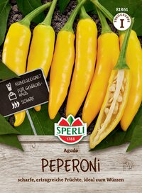 Gelbe Peperoni, eine halb aufgeschnitten, auf dunklem Boden, mit grünen Blättern im Hintergrund.