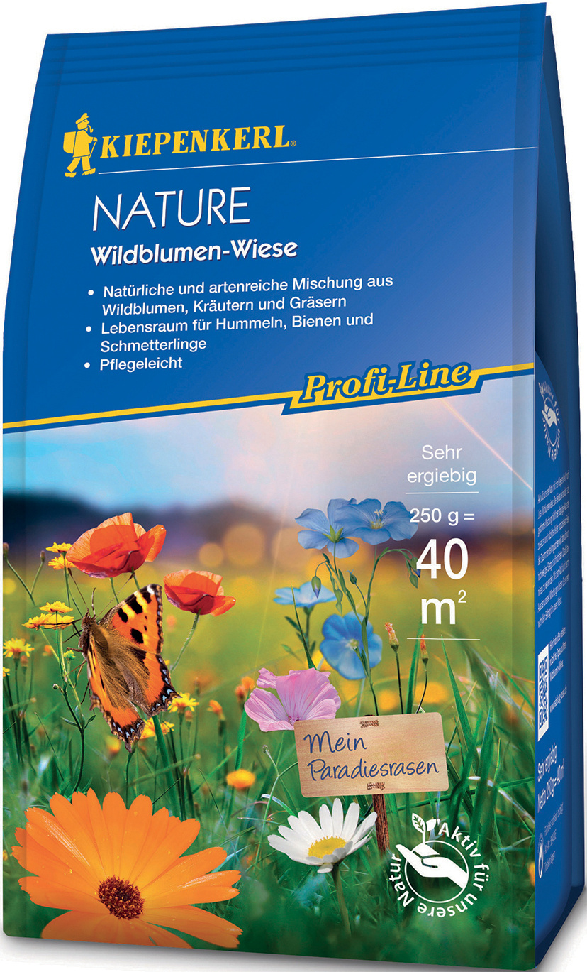 Bunte Blumen mit Schmetterling und einer kleinen Tafel mit der Aufschrift "Mein Paradiesrasen" vor blauem Himmel.
